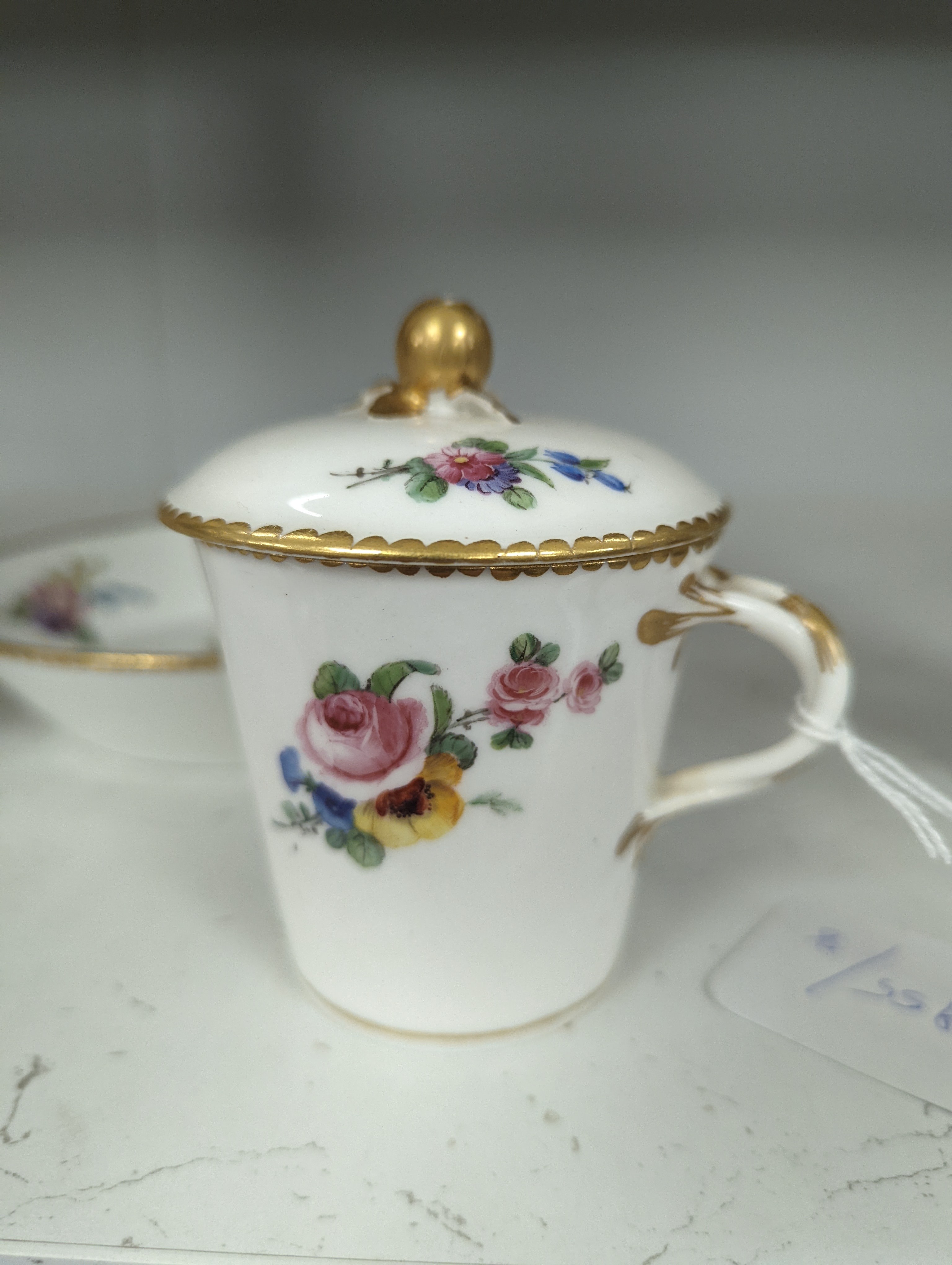 A Sevres tapering cup with entwined handle and cover and stand painted with flowers, date code for 1780, painters mark for Le Bel jnr., square incised marks, height 10.5cm